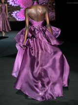 Vestido largo de fiesta realizado en organza de seda color morado. Destaca el elegante juego de plisados que envuelve el cuerpo, creando el elegante cuello halter del diseño. El contrapunto perfecto a la voluminosa falda del vestido, que aporta dinamismo y movimiento de Hannibal Laguna