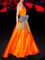 Vestido de fiesta en mikado color naranja, cuerpo drapeado asimétrico, falda cruzada y cinturón azul noche de HANNIBAL LAGUNA.