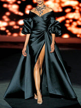 Vestido de fiesta realizado en matelé negro con escote liz cruzado, maxi mangas abullonadas y falda compuesta de sirena con pliegues y amplia cola de Hannibal Laguna