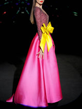 Vestido de fiesta largo en mikado pique fresa y lentejuelas granate, t-shirt con escote V con manga larga y amplia falda de capa cruzada. Cinturón lazo en color lima de HANNIBAL LAGUNA.