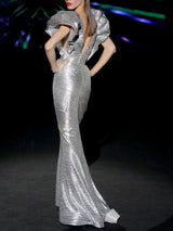 Vestido de fiesta en lamé plata plisado, cuerpo escote en V, mangas XXL abullonadas y falda sirena entallada de HANNIBAL LAGUNA.