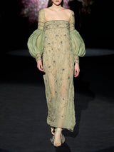 Vestido largo evasé con escote palabra realizado en gasa verde olivo bordado con diminutos cristales y cuenta con brillantes bordados de inspiración floral, maxi mangas en garza plisada verde olivo de Hannibal Laguna