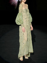 Vestido largo evasé con escote palabra realizado en gasa verde olivo bordado con diminutos cristales y cuenta con brillantes bordados de inspiración floral, maxi mangas en garza plisada verde olivo de Hannibal Laguna