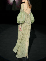 Vestido largo evasé con escote palabra realizado en gasa verde olivo bordado con diminutos cristales y cuenta con brillantes bordados de inspiración floral, maxi mangas en garza plisada verde olivo de Hannibal Laguna