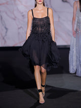 Vestido corto con falda asimétrica de gasa de seda negra con cuerpo bordado formando flecos con lentejuelas ovaladas y escote cuadrado de Hannibal Laguna