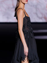 Vestido corto con falda asimétrica de gasa de seda negra con cuerpo bordado formando flecos con lentejuelas ovaladas y escote cuadrado de Hannibal Laguna