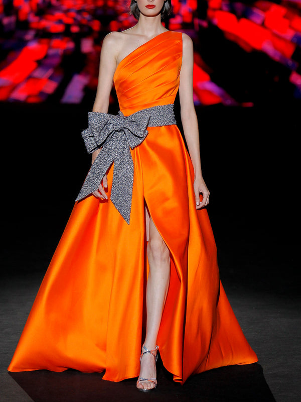 Vestido de fiesta en mikado color naranja, cuerpo drapeado asimétrico, falda cruzada y cinturón azul noche de HANNIBAL LAGUNA.